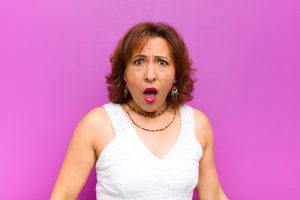 woman looking shocked, annoyed or disappointed, open mouthed against purple backdrop