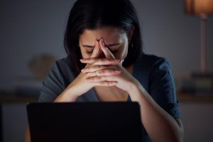 Woman sitting over a laptop, hands locked with anxiety.
