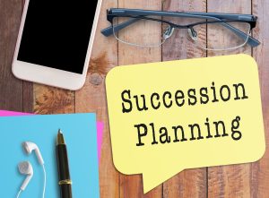 Succession planning text on notebook with glasses, pen, and iphone on table