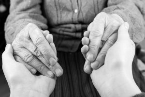 black and white image of someone holding the hands of an elderly man.